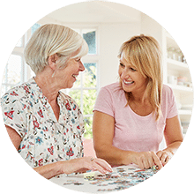 A middle aged woman sitting next to an elderly woman both happily working on a jigsaw puzzle