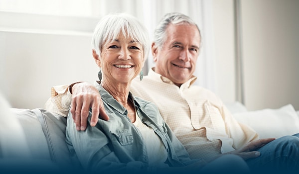 An elderly couple sitting on a couch together smiling