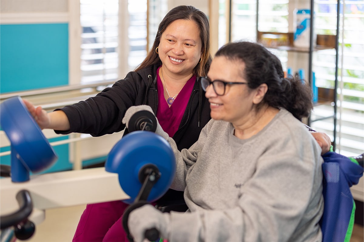 All Saints Post Healthcare physical therapist assisting resident on rehab machine